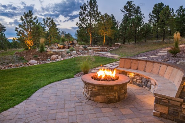 Backyard fire pit with stone seating and a landscaped garden in the background.
